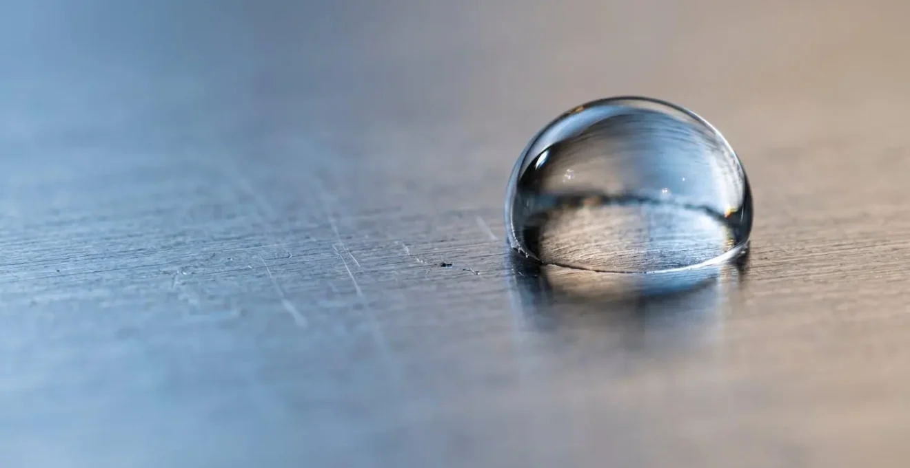 Gros plan macro d'une goutte d'eau sur une surface métallique industrielle montrant la tension de surface